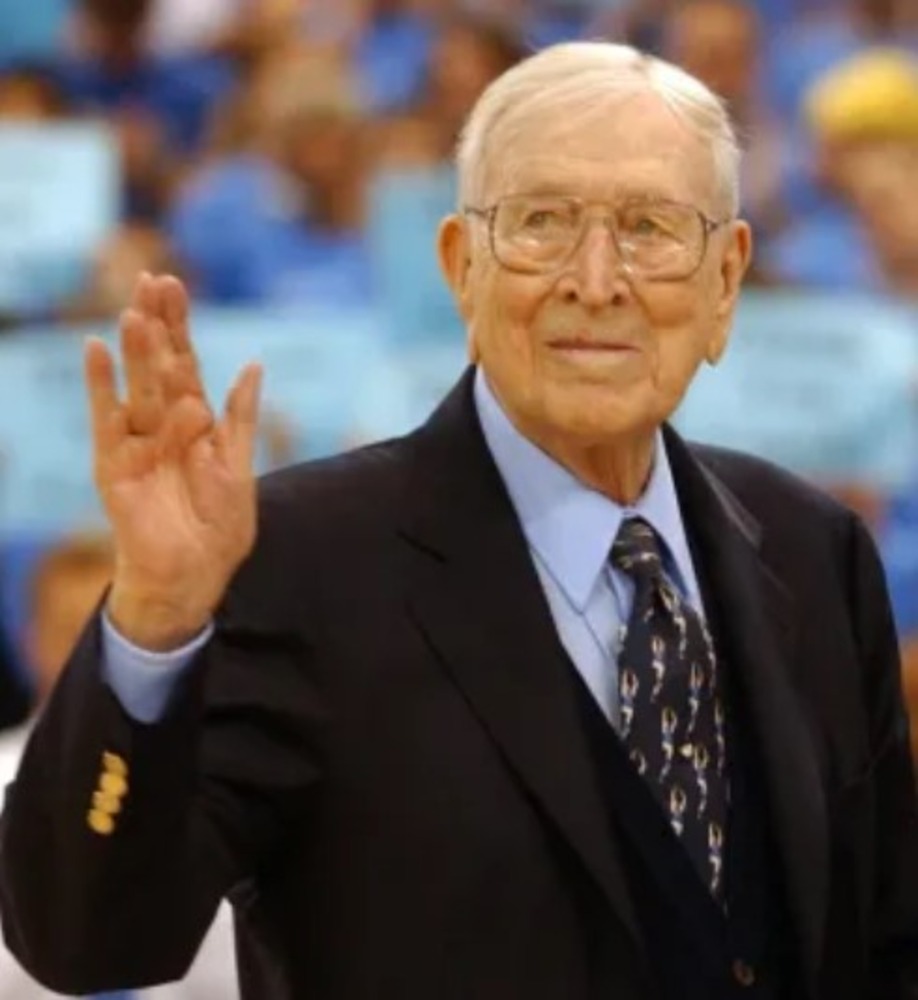 Coach Wooden in a suit, waiving.